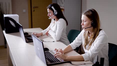 Mehrere-Frauen-druckt-den-Text-auf-der-Laptoptastatur,-die-Damen-Vortrag-über-das-Mikrofon-im-Call-Center-Büro,-sie-eingehende-Anrufe-beantworten-und-beraten-Kunden