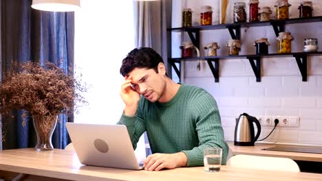 Depressed-Man-Upset-by-Loss-Working-on-Laptop,-Sitting-in-Kitchen