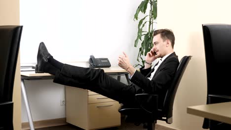 Young-man-sitting-in-office,-talking-on-mobile-phone-and-squeezes-hand-expander.-60-fps