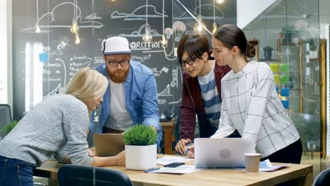 Team-Treffen-von-Entwicklern,-sie-lehnen-sich-an-den-Tisch-und-schauen-Sie-sich-die-Ergebnisse-auf-dem-Laptop.-Junge-kreative-in-stilvollen-Büroumgebung.