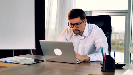 A-businessman-sits-at-his-desk-and-types-on-a-laptop.