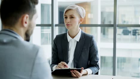 HR-businesswoman-having-job-interview-with-young-man-in-suit-and-watching-his-resume-application-in-modern-office