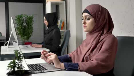 Two-young-beautiful-girls-in-hijabs-work-in-the-office,-on-computers.-Arab-women-in-the-office.-fucus-pull-60-fps