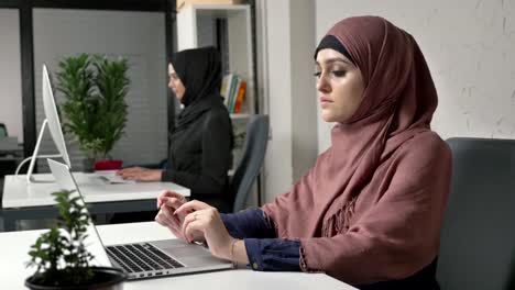 Dos-jóvenes-chicas-guapas-en-hijabs-trabajan-en-la-oficina,-en-los-equipos.-Mujeres-árabes-en-la-oficina.-Fucus-tire-60fps