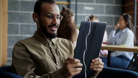 African-american-man-in-glasses-holding-smartphone-and-have-online-video-call-while-his-colleagues-working-in-modern-office