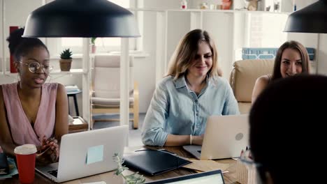 Young-happy-beautiful-multiethnic-female-colleagues-discuss-business-by-office-table-in-stylish-loft-coworking-space-4K