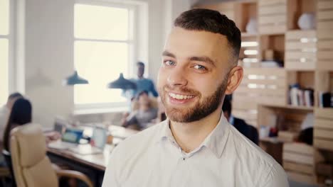 Portrait-of-young-happy-Caucasian-businessman-posing-at-busy-office.-Handsome-male-creative-worker-looking-at-camera-4K