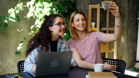 Fröhlichen-Kolleginnen-machen-Selfie-mit-Smartphone-und-entspannen-im-Arbeitsplatz,-dann-beobachten-und-prüfen-Fotos-zusammen.-Büro-Spaß-Konzept.