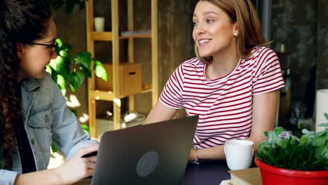 Young-female-enterpreneurs-sitting-together-at-table-and-talking-emotionally.-Women-are-wearing-casual-clothes-and-stylish-accessories.