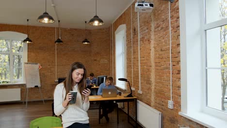 Schöne-Frau-Kaffee-trinken-mit-Smartphone-im-modernen-Loft-Büro