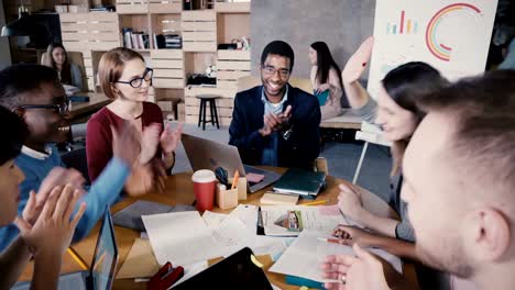 Multiethnic-group-celebrates-success-at-meeting.-Young-happy-business-employees-clap,-give-high-fives-and-raise-arms-4K