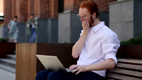 Erstaunt-Fragen,-Designer-mittels-Laptop-sitzend-auf-Bank