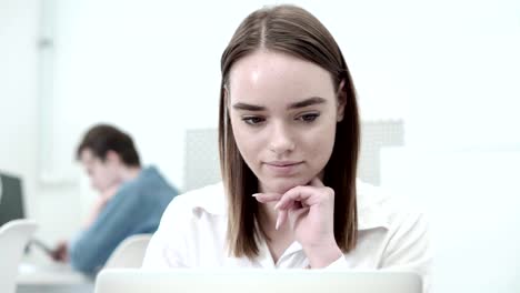 Primer-plano-de-hermosa-alumna-leyendo-en-la-pantalla-del-ordenador-portátil-y-sonriente,-su-estudiante-del-compañero-en-teléfono-de-fondo