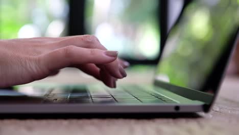 Manos-de-una-mujer-trabajando-y-escribiendo-en-el-teclado-del-ordenador-portátil-en-la-mesa-de-madera