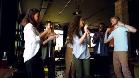 Entusiasmados-jóvenes-hombres-y-mujeres-compañeros-de-trabajo-están-bailando-y-haciendo-victoria-celebrando-chocan-en-el-trabajo.-Diversión-de-la-oficina,-eventos-corporativos-y-concepto-de-estilo-de-vida-moderno.