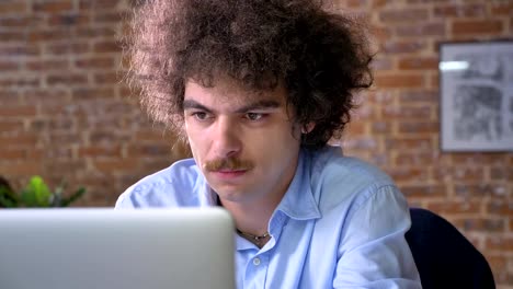 Stressed-worker-with-curly-hair-and-mustache-holding-his-head,-problems-with-business,-modern-office-background