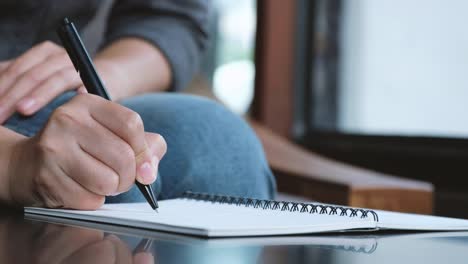 Die-Hand-einer-Frau-auf-einem-weißen-leeren-Notebook-auf-Tabelle-aufschreiben