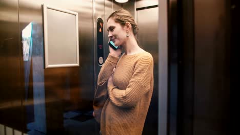 Una-vista-de-relajado-Europea-joven-montar-encima-en-elevador-de-la-pared-de-cristal-transparente-hablando-por-teléfono-y-sonriendo