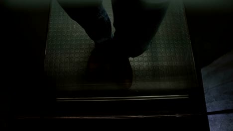 Young-European-man-in-brown-shoes-riding-elevator-up,-walking-out,-seen-through-transparent-glass-wall,-high-angle-view
