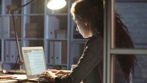 Junge-weibliche-Büroangestellte-schreiben-auf-Computer-in-der-Nacht