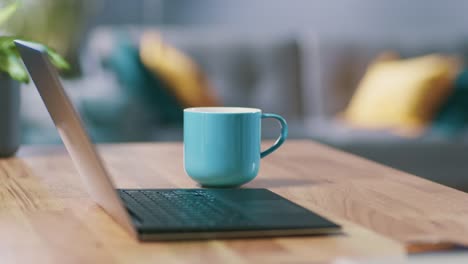 Anonymous-Man-Enters-His-Living-Room-with-a-Mug-and-Sits-Down-at-His-Desk-Starts-Working-on-a-Laptop.