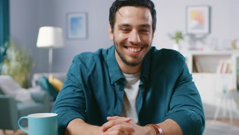 Portrait-of-Handsome-Man-Sitting-at-Desk-in-His-Living-Room-and-Charmingly-Smiling.-Medium-Shot.