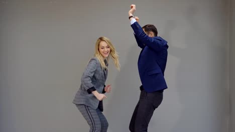 joyful-woman-and-man-in-business-suits-dancing-on-grey-background