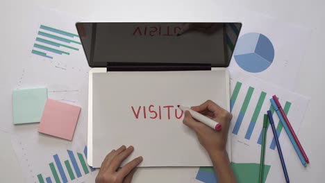 Business-concept.-Woman-writing-VISITORS-on-paper-on-office-desktop.