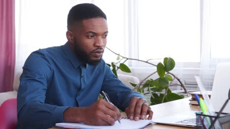 Businessman-using-laptop-and-taking-notes-at-office