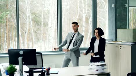 Hübsche-Geschäftsfrau-lehrt-ihren-männlichen-Kollegen-zu-tanzen,-Musik-hören-und-bewegen-im-Büro-Pause-von-der-Arbeit-zu-genießen.-Die-Menschen-sind-Anzüge-tragen.