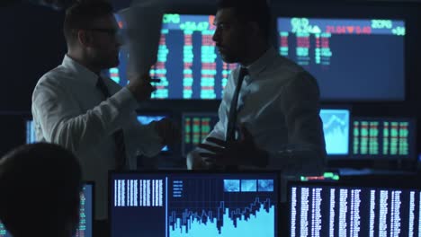 Two-stockbrokers-are-having-an-argument-at-work-in-a-dark-office-with-display-screens.