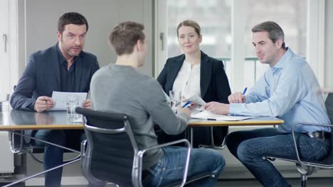 Three-businesspeople-consults-a-younger-men-at-a-meetingroom