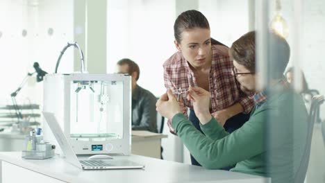 Engineers-Use-3D-Printer-and-Discuss-Printed-Component.-Their-Coworkers-Work-in-Background.-Their-Location-is-Bright-Modern-Office.