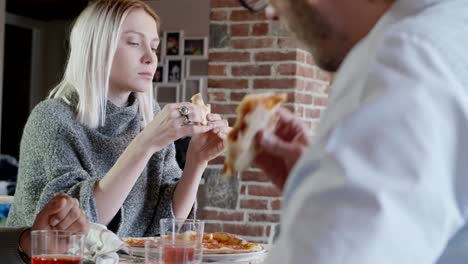 Grupo-multiétnico-de-amigos-personas-disfrutar-de-almuerzo-o-cena-comida-a-comer-pizza-interior-en-casa-moderna-industrial.-Foto-video-de-4-k-mano-lenta