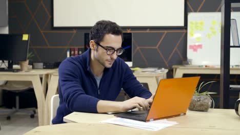 Creative-man-in-glasses-using-laptop-at-workplace