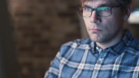 Young-man-in-glasses-is-sitting-in-front-of-a-monitor-in-a-loft-and-working.