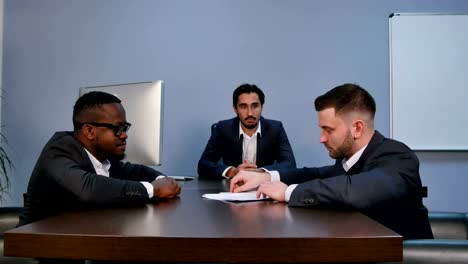 Young-serious-man-holding-papers,-reading-them-attentively,-during-meeting-in-office