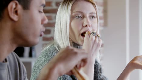 Grupo-multiétnico-de-amigos-personas-disfrutar-de-almuerzo-o-cena-comida-a-comer-pizza-interior-en-casa-moderna-industrial.-cerca-de-4-k-mano-lenta-toma-video