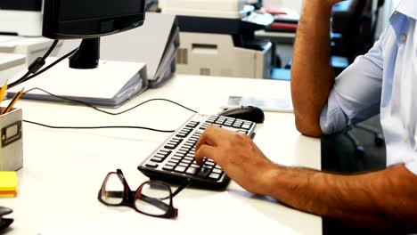 Male-executive-using-mobile-phone-while-working-on-computer