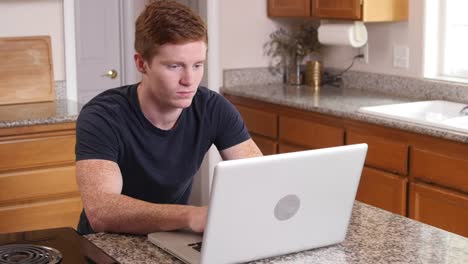 Young-man-working-on-computer-in-kitchen