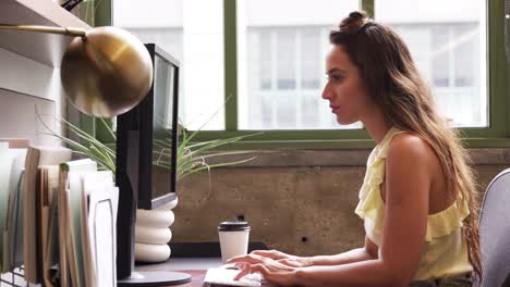 Junge-weiße-Frau,-die-mit-Computer-in-einem-Büro,-Seitenansicht