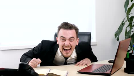 Young-businessman-in-suit-sitting-in-office-and-laughing-hysterically-60-fps