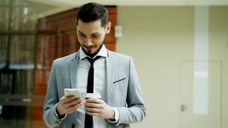 Stedicam-shot-of-cheerful-businessman-using-smartphone-and-walking-in-modern-office-hall