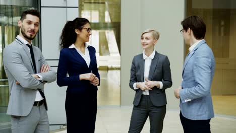 Portrait-of-group-of-business-people-talking-and-then-smiling-looking-into-camera-in-modern-office-hall-indoors