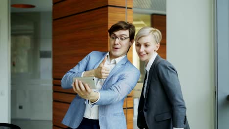 Happy-businessman-and-his-female-colleague-taking-a-selfie-on-smarphone-camera-for-social-media-in-modern-office