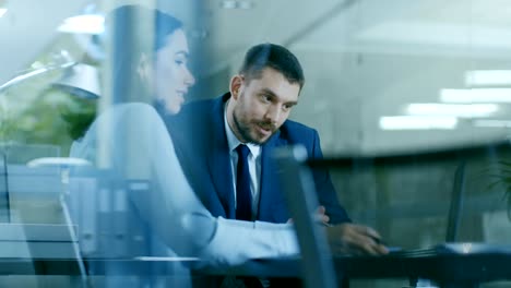 Schöne-weibliche-Manager-hat-Diskussion-mit-einem-Geschäftsmann-sitzt-an-seinem-Schreibtisch.-Arbeiten-an-Deal-teilen-sie-einen-Laptop-im-modernen-Büro.