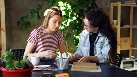 Team-of-two-creative-designers-are-looking-at-pictures-and-talking-about-them-while-sitting-together-at-desk.-Pan-shot-of-modern-informal-office.-Friendly-working-atmosphere.