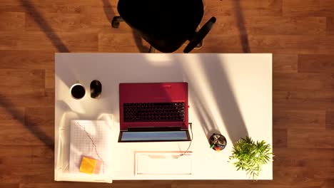 Young-man-in-glasses-and-suit-sitting-behind-desk-with-laptop-and-coffee,-going-away,-top-shot