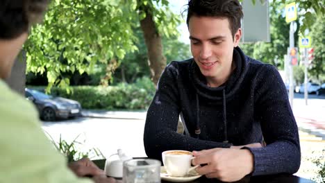 Junge-Mann-im-Gespräch-mit-Freund-beim-Sitzen-im-Cafe-Terrasse