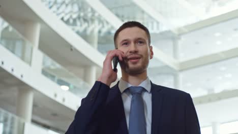 Junger-Mann-zu-Fuß-und-sprechen-auf-dem-Handy-im-Business-Center